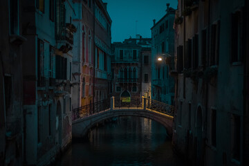 Fototapeta na wymiar Beautiful small bridge with yellow lighting over a canal in magnificent city of Venice during night time or early evening. Blue hour in Venice, Italy.