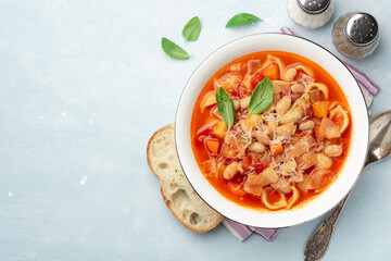 Italian minestrone soup with parmesan cheese and basil on blue concrete background