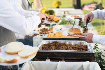 Close up of bridal party dishing up catered buffet food at casual outdoor wedding