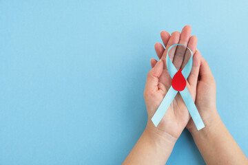 Womans hands hold light blue ribbon awareness with red blood drop. World diabetes day. Top view, copy space