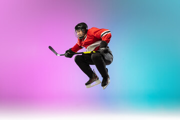 Obraz premium In jump. Male hockey player with the stick on ice court and neon gradient background. Sportsman wearing equipment, helmet practicing. Concept of sport, healthy lifestyle, motion, wellness, action.