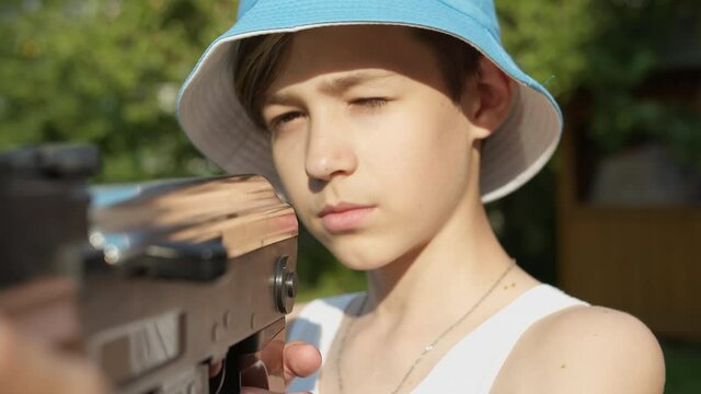 portrait of a serious boy reloading a kalashnikov assault rifle outdoors