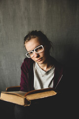 Girl in glasses with a book on a gray background. The girl is holding an old book.