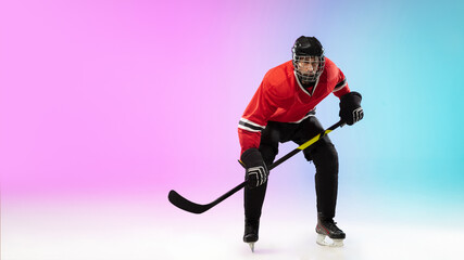 Fototapeta premium Attack. Male hockey player with the stick on ice court and neon gradient background. Sportsman wearing equipment, helmet practicing. Concept of sport, healthy lifestyle, motion, wellness, action