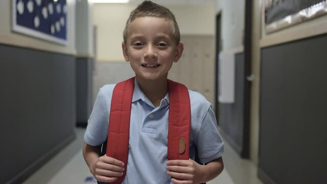 Elementary or Primary school boy with backpack smiles at camera in school hall