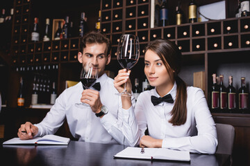 Selective focus of sommelier holding glass of wine near colleague and notebooks on table