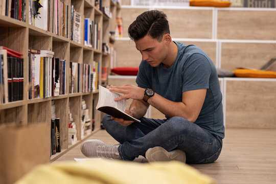 	
Young male student read and learns by the book shelf at the library.Reading a book.	
