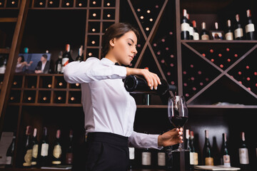 Brunette sommelier pouring wine from bottle in restaurant