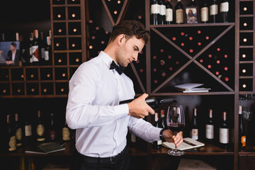 Young sommelier pouring wine in glass in restaurant