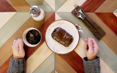 Dessert and cappuccino, male hands in the frame.
Chocolate baking with poppy seeds lies on a saucer in the foreground. Breakfast in the cafe, a croissant and a drink are shown on the designer desk.
