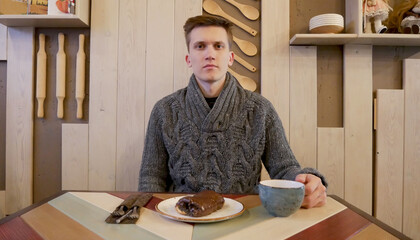 Guy is sitting in a cafe and drinking cappuccino. Chocolate baking with poppy seeds lies on a saucer in the foreground. Breakfast in the cafe, croissant and drinks are shown.