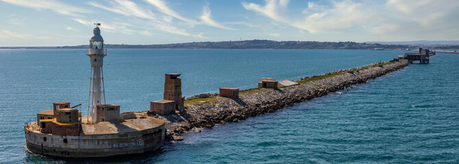 Naklejka premium Lighthouse and water barrier at the entrance to the Portland harbour in Weymouth Bay, UK