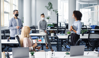 Report on work, meeting or team building during covid-19 outbreak. Young african american lady with tablet speaks to colleagues in modern office interior