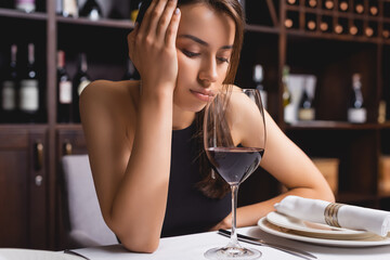 Sad woman looking at glass of wine at table in restaurant