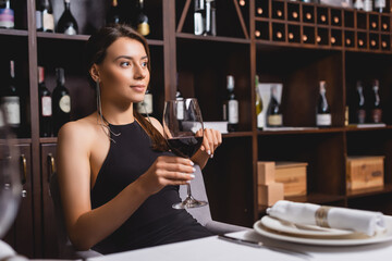Selective focus of elegant woman holding glass of wine at table in restaurant