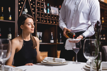 Selective focus of sommelier pouring wine in glass near young woman in restaurant - Powered by Adobe