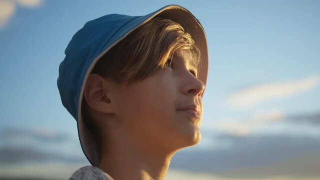 portrait of a happy boy in a hat looking at the beautiful blue sky, sun glare