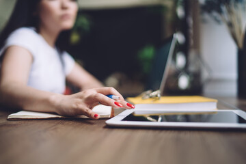 Crop female freelancer using tablet and taking notes at home