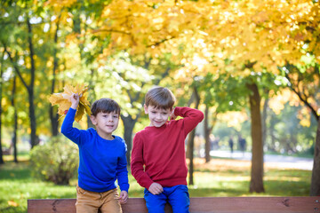 happy friends, schoolchildren having fun in autumn park among fallen leaves