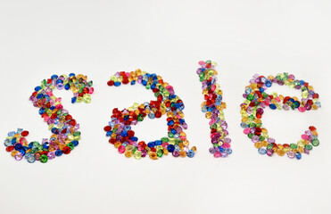The inscription "sale". It is laid out with glass beads on a white background. Close up.