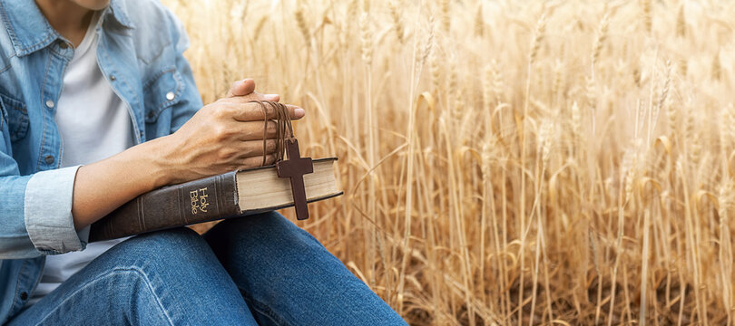 Christian woman praying on holy bible and wooden cross in barley field on summer. Woman pray for god blessing to wishing have a better life and believe in goodness.