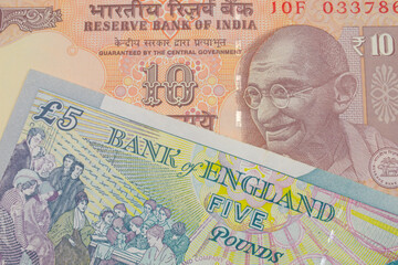 A macro image of a orange ten rupee bill from India paired up with a colorful, five pound bank note from the United Kingdom.  Shot close up in macro.
