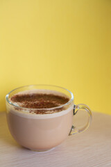a mug of coffee with milk sprinkled with chocolate chips, and foam, on a yellow background. Energy and cheerfulness in the morning.
