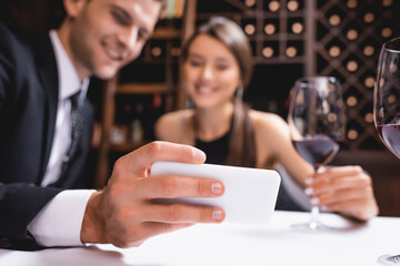 Selective focus of young couple looking at smartphone near glasses of wine in restaurant