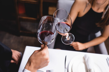 Cropped view of young couple clinking with classes of wine in restaurant