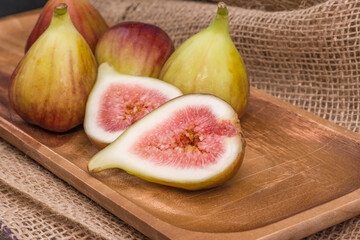 Fresh fig sliced in half with whole figs in the background, on a wooden surface.