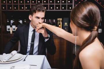 Selective focus of man in formal wear kissing hand of girlfriend during dating in restaurant