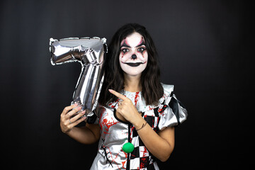 woman in a halloween clown costume over isolated black background holding a number seven balloon. Anniversary