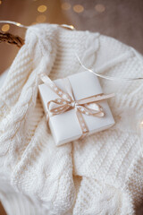 Fototapeta na wymiar small white gift box with ribbon, knitted sweater, wicker basket, Christmas lights.