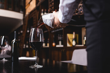 Cropped view of young sommelier pouring wine in glass in restaurant