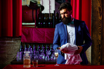 Barman pouring champagne in champagne glass. Bearded handsome man holding glass of wiskey.