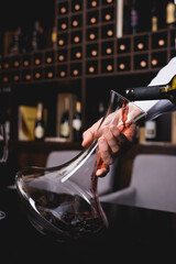 Cropped view of sommelier pouring red wine in decanter on table