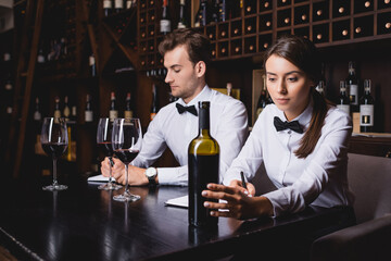 Selective focus of sommeliers noticing on notebooks near bottle and glasses of wine in restaurant