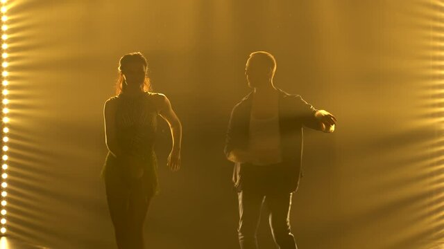 A couple of young dancers dancing a passionate Latin American salsa dance surrounded by yellow lights. Silhouettes of a man and a woman move their hips to the beat of the music. Close up.