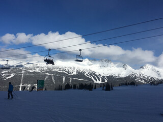 Landscape view of skiers on a chairlift silhouetted against the bright snow covered mountains of whistler mountain on a sunny day