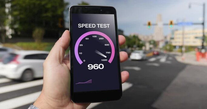 A man in the Oakland district of Pittsburgh tests his cellular download bandwidth speed on a mobile phone. Traffic and taxi cabs pass in background. Fictional interface speedometer gauge created in AE