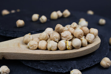 Macro closeup of isolated wood spoon with raw uncooked chickpeas (channa dhal) on black slate stone background