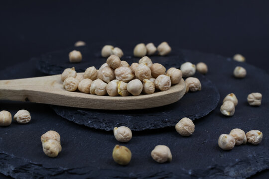 Macro closeup of isolated wood spoon with raw uncooked chickpeas (channa dhal) on black slate stone background