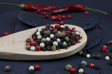 Macro closeup of isolated dried green, black and red mixed peppercorns with isolated wood spoon on slate stone background (focus on center)