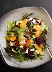 Salad with arugula, orange, beet, cheese, pomegranate seeds and nuts on a gray plate on a black background. Background image, copy space