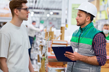 side view on supervisor and customer discussing in store, worker in uniform consult caucasian man