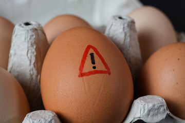Closeup of isolated raw brown eggs in carton box with warning sign - salmonella infection risk and...
