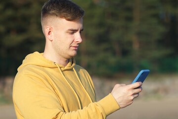 Serious young man looking at his cell mobile phone. Guy is typing a message on his smartphone outdoors