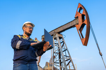 Engineer with a laptop against the background of oil rockers.