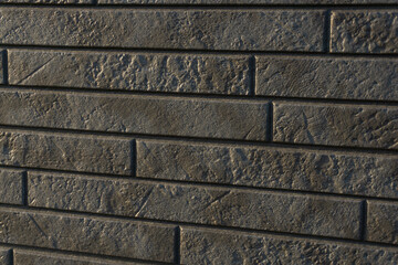 A wall of shiny, rough black bricks reflecting the sun.