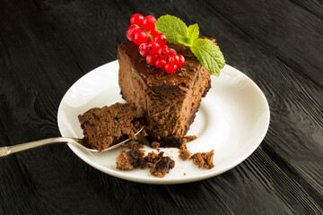 A piece of chocolate cheesecake on the white plate on the black wooden background closeup
